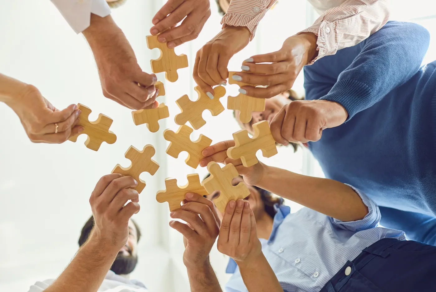 A group of people fitting wooden puzzle pieces together, representing a collaborative approach